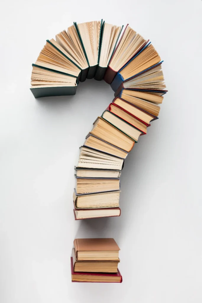 Una pila de libros de colores forma un signo de interrogación sobre un fondo blanco.