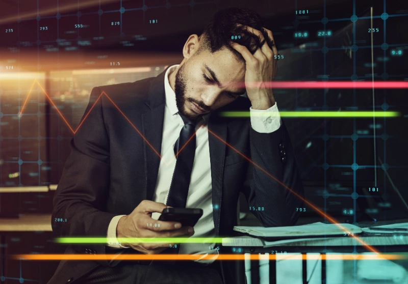 Hombre de negocios preocupado mirando su teléfono frente a gráficos financieros superpuestos.