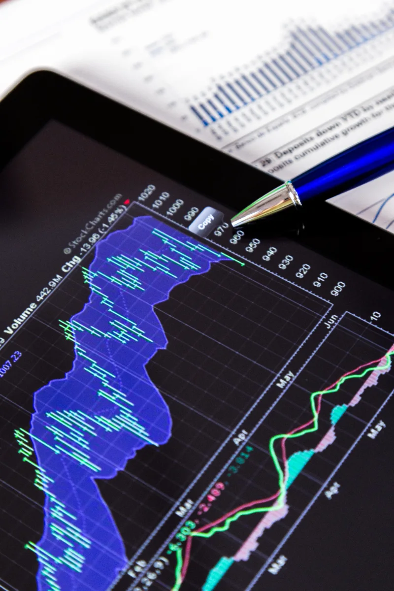 Tablet mostrando gráficos financieros junto a documentos de análisis de mercado