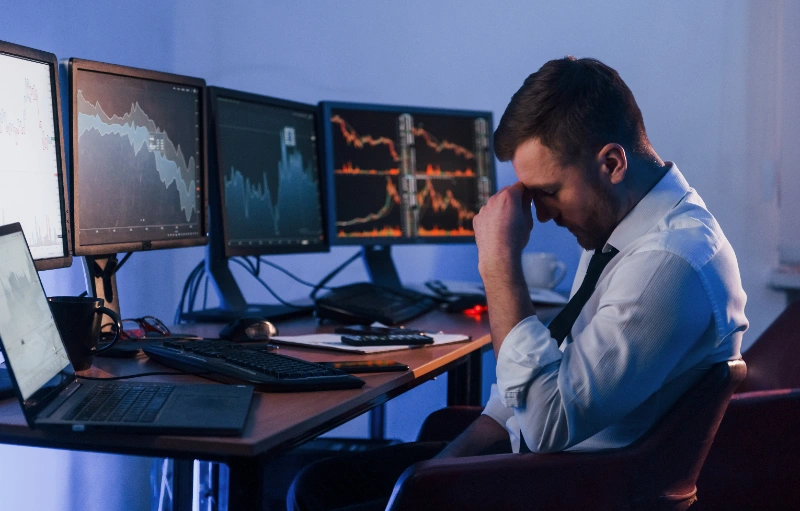 Inversionista o trader estresado frente a múltiples monitores con gráficos bursátiles.