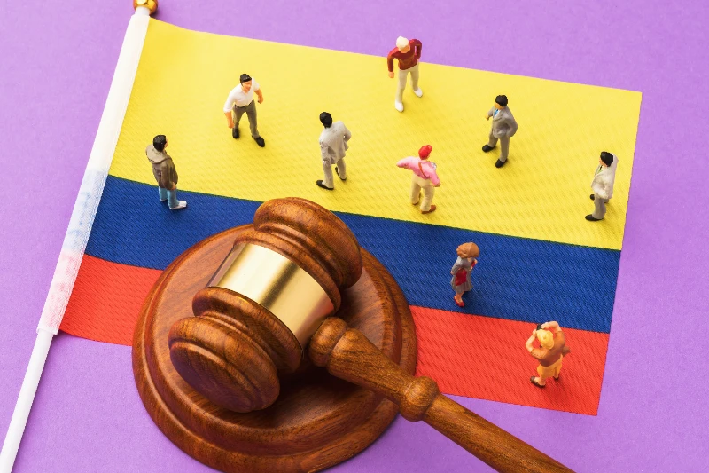 Un mazo de juez de madera y pequeñas figuras en miniatura dispuestas sobre la bandera de Colombia, simbolizando la justicia y el sistema legal en la sociedad.
