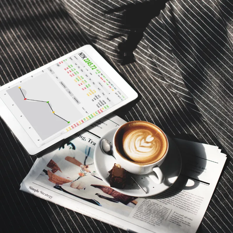Una tablet con datos bursátiles descansa sobre un periódico junto a una taza de café en una superficie con textura.