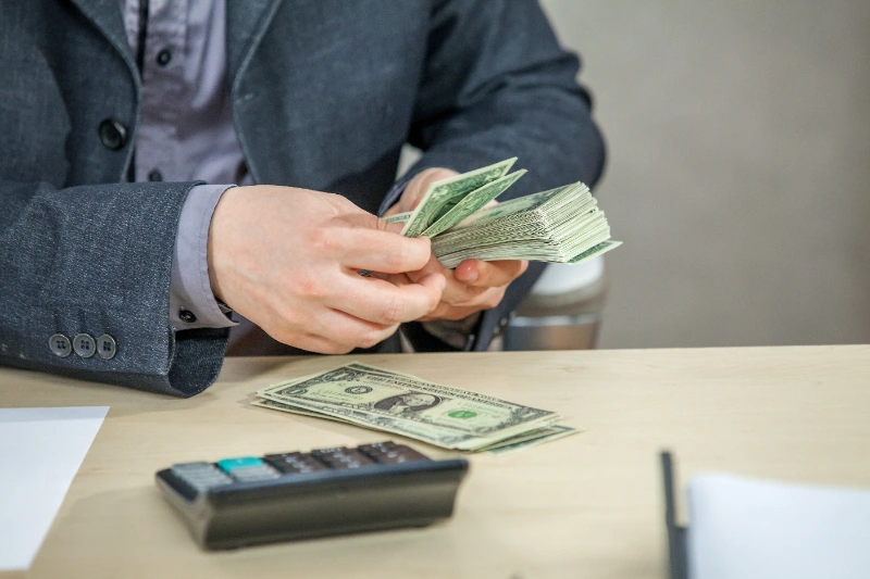 Un empresario cuenta un taco de billetes de dólar en su escritorio junto a una calculadora.